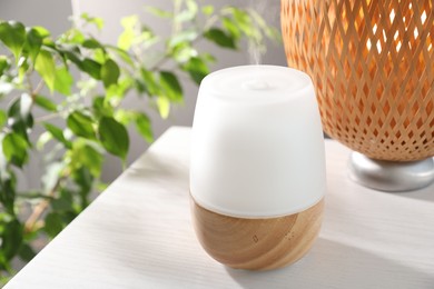 Photo of Modern aroma lamp on white wooden table indoors, closeup
