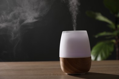 Photo of Modern aroma lamp on wooden table indoors. Space for text