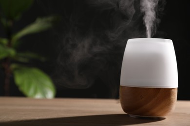 Photo of Modern aroma lamp on wooden table indoors. Space for text