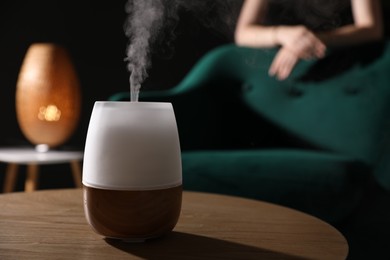 Photo of Woman near armchair indoors, focus on modern aroma lamp