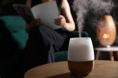 Photo of Woman reading magazine in armchair indoors, focus on modern aroma lamp