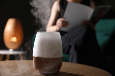 Photo of Woman reading magazine in armchair indoors, focus on modern aroma lamp