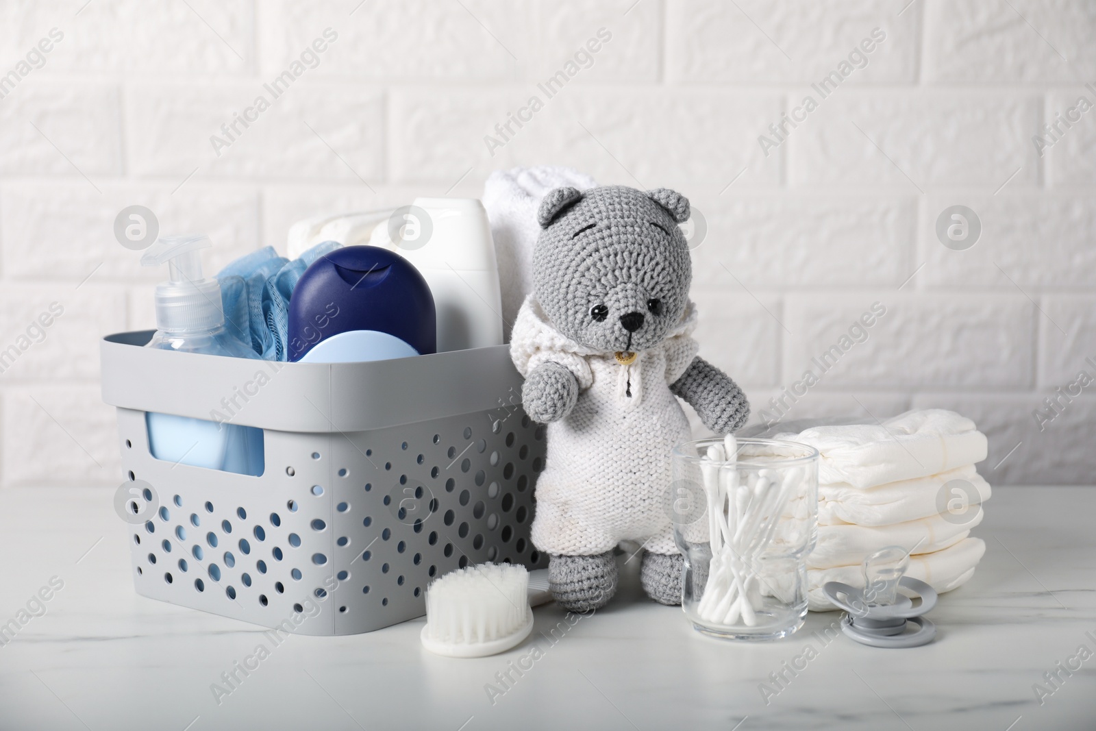 Photo of Many different baby accessories and toy bear on table near brick wall