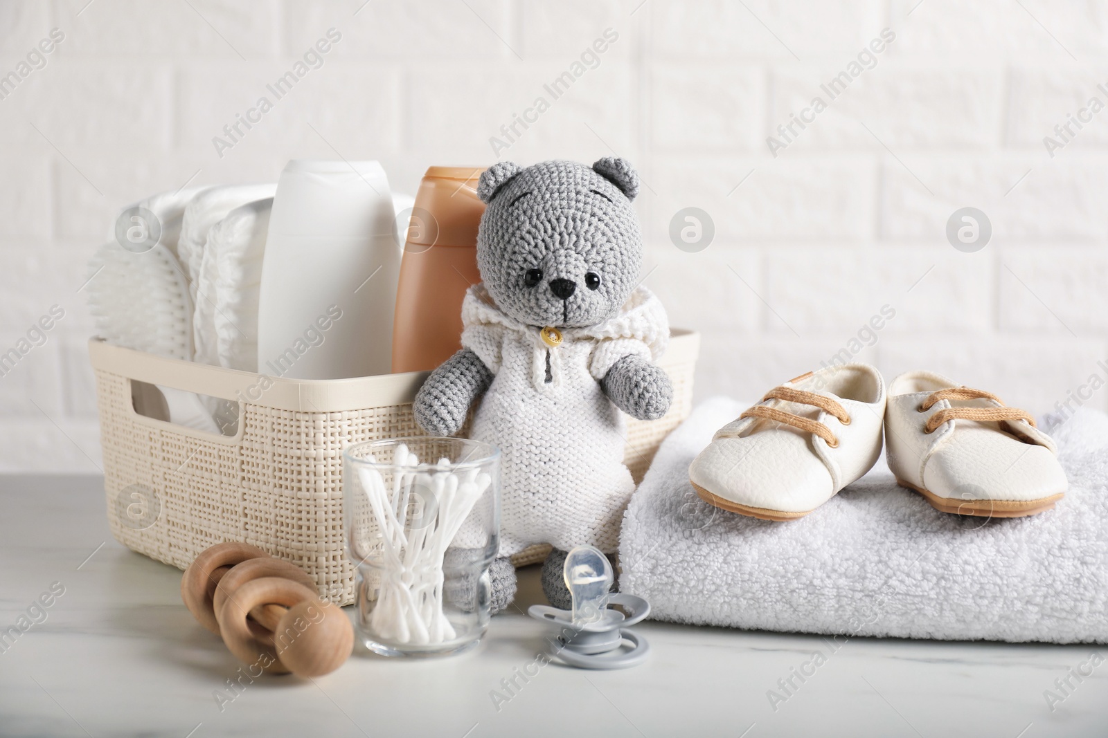Photo of Many different baby accessories and toy bear on table near brick wall