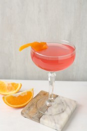 Photo of Martini cocktail with garnish and slices of orange on white table, closeup