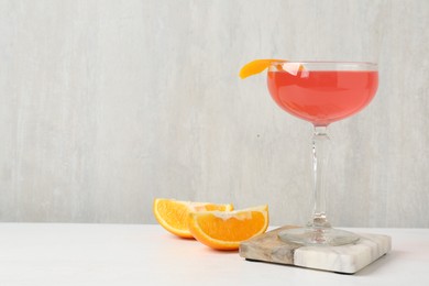Photo of Martini cocktail with garnish and slices of orange on white table, space for text