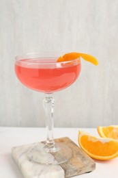 Photo of Martini cocktail with garnish and slices of orange on white table, closeup