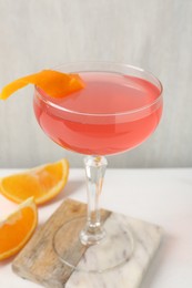 Photo of Martini cocktail with garnish and slices of orange on white table, closeup