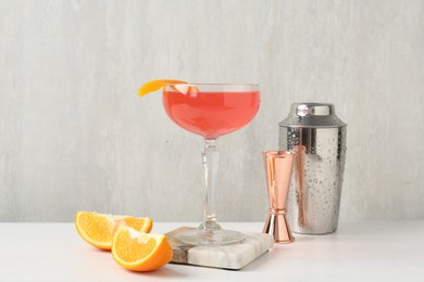 Photo of Martini cocktail with garnish, slices of orange and bartender equipment on white table