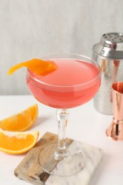 Photo of Martini cocktail with garnish, slices of orange and bartender equipment on white table, closeup