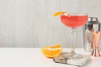 Photo of Martini cocktail with garnish, slices of orange and bartender equipment on white table, closeup. Space for text