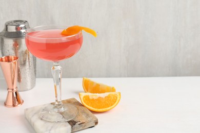 Photo of Martini cocktail with garnish, slices of orange and bartender equipment on white table, closeup. Space for text