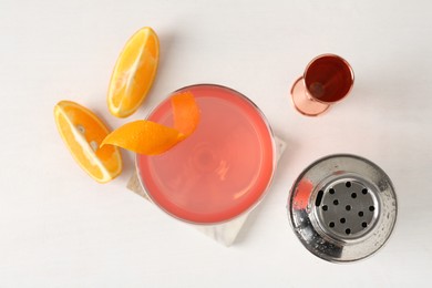 Photo of Martini cocktail with garnish, slices of orange and bartender equipment on white table, flat lay