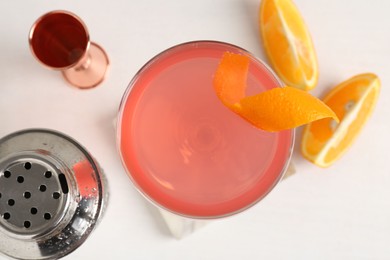 Photo of Martini cocktail with garnish, slices of orange and bartender equipment on white table, flat lay