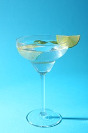 Photo of Martini cocktail with slices of lime and mint on light blue background, closeup