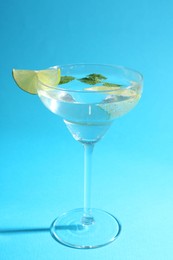 Photo of Martini cocktail with slices of lime and mint on light blue background, closeup
