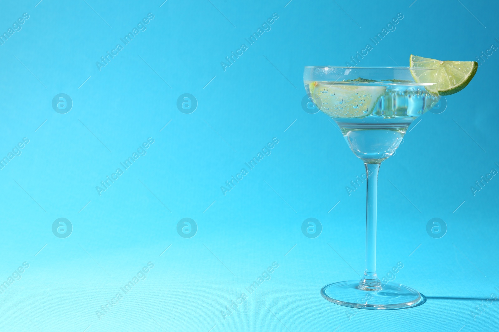 Martini cocktail with slices of lime and mint on light blue background, space for text Photo of Martini cocktail with slices of lime and mint on light blue background, space for text
