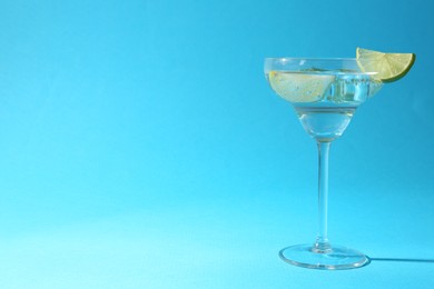 Photo of Martini cocktail with slices of lime and mint on light blue background, space for text