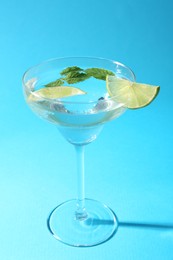 Photo of Martini cocktail with slices of lime and mint on light blue background, closeup