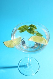 Photo of Martini cocktail with slices of lime and mint on light blue background, closeup