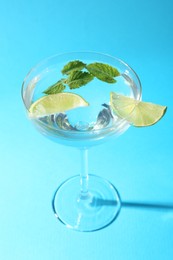 Photo of Martini cocktail with slices of lime and mint on light blue background, closeup