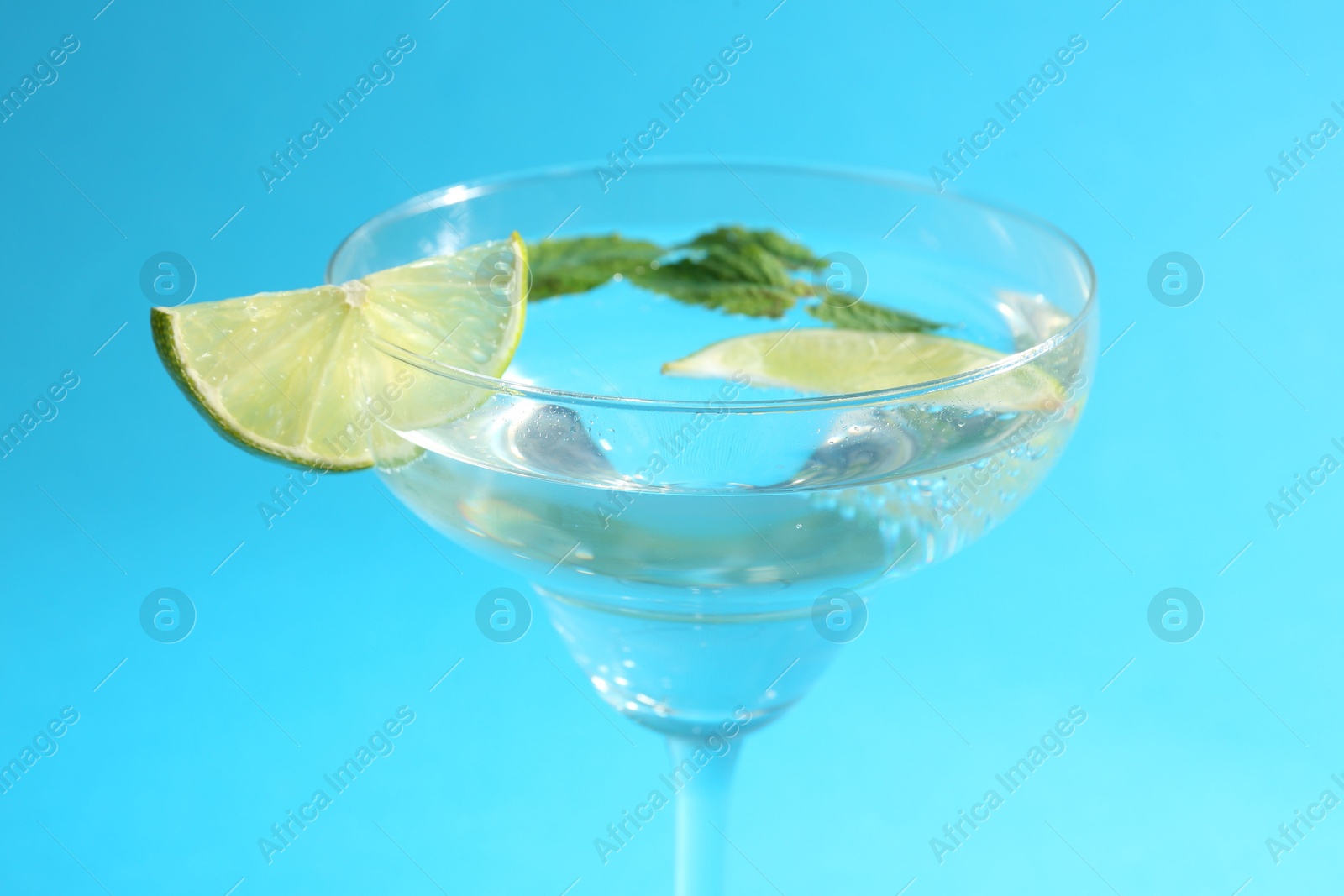 Martini cocktail with slices of lime and mint on light blue background, closeup Photo of Martini cocktail with slices of lime and mint on light blue background, closeup