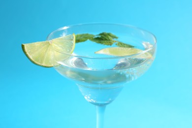 Photo of Martini cocktail with slices of lime and mint on light blue background, closeup