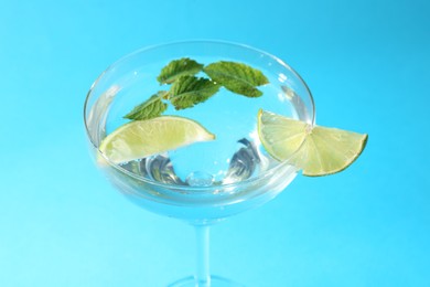 Photo of Martini cocktail with slices of lime and mint on light blue background, closeup