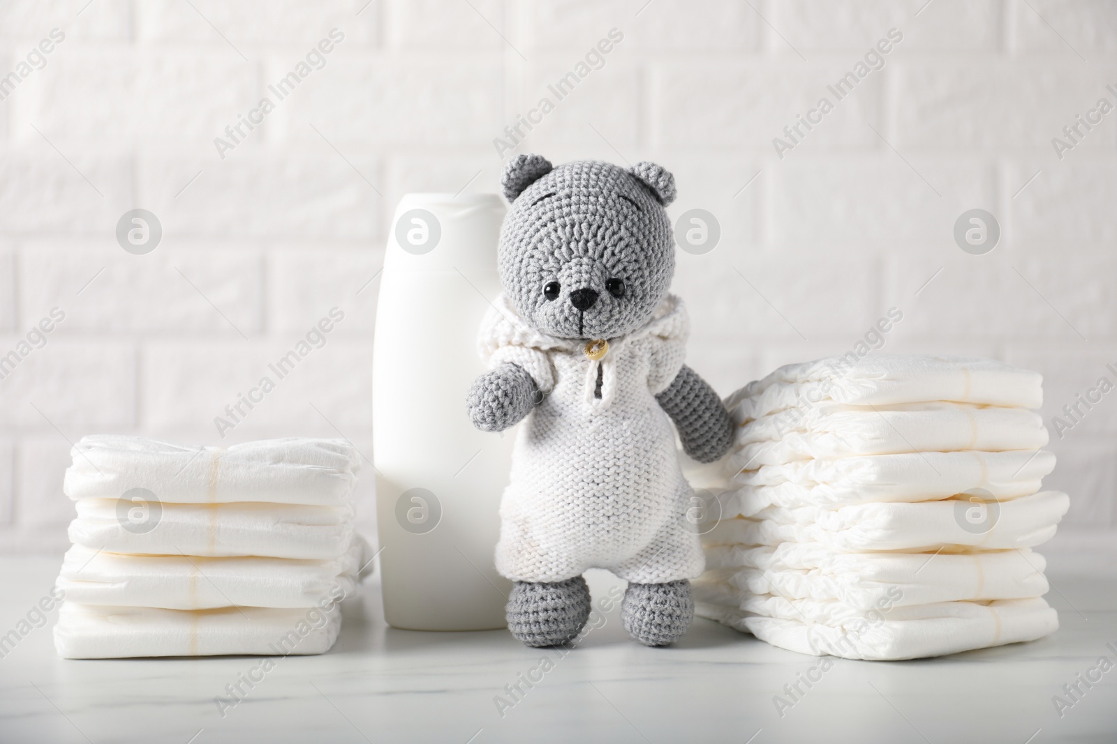 Photo of Baby diapers, shampoo and toy bear on white table near brick wall
