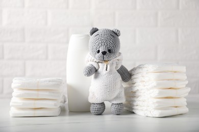 Photo of Baby diapers, shampoo and toy bear on white table near brick wall