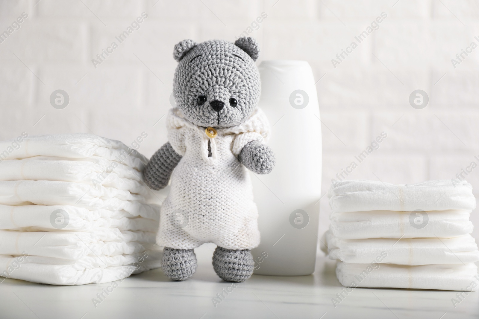 Photo of Baby diapers, shampoo and toy bear on white table near brick wall
