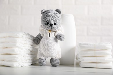 Photo of Baby diapers, shampoo and toy bear on white table near brick wall