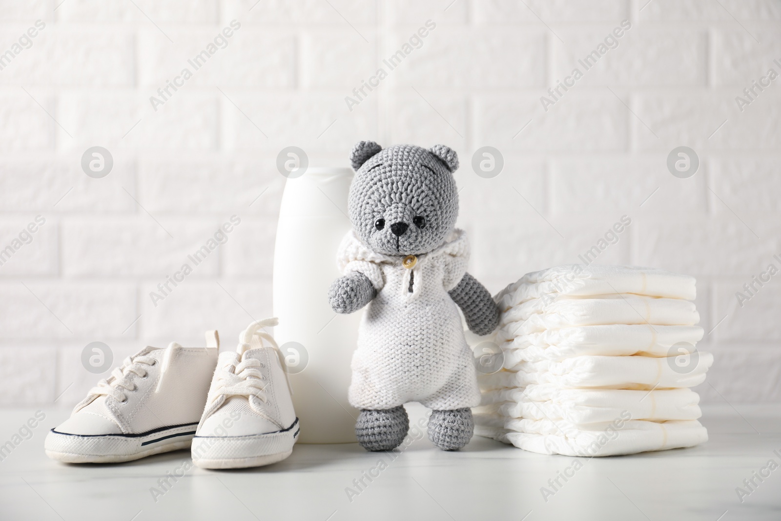 Photo of Many different baby accessories and toy bear on table near brick wall