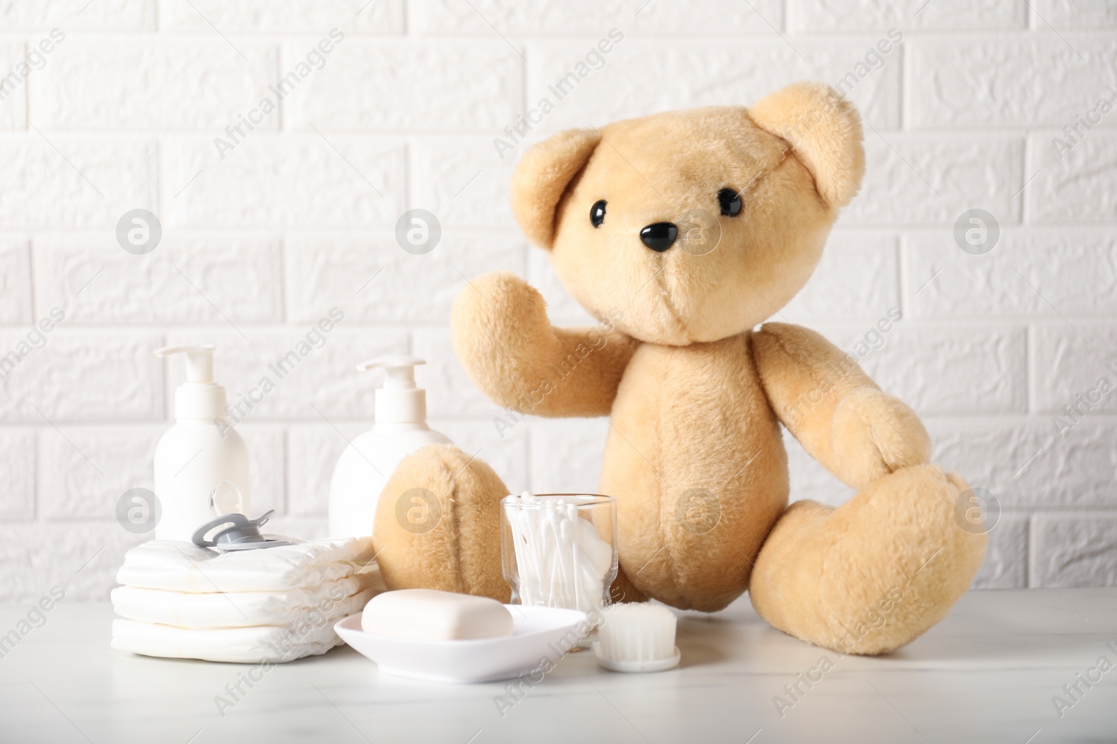 Photo of Many different baby accessories and toy bear on table near brick wall