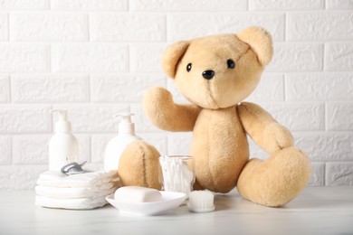 Photo of Many different baby accessories and toy bear on table near brick wall