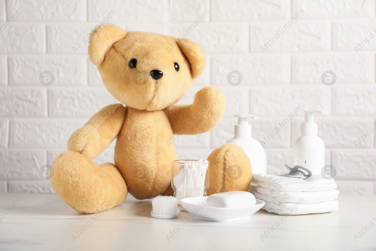 Photo of Many different baby accessories and toy bear on table near brick wall