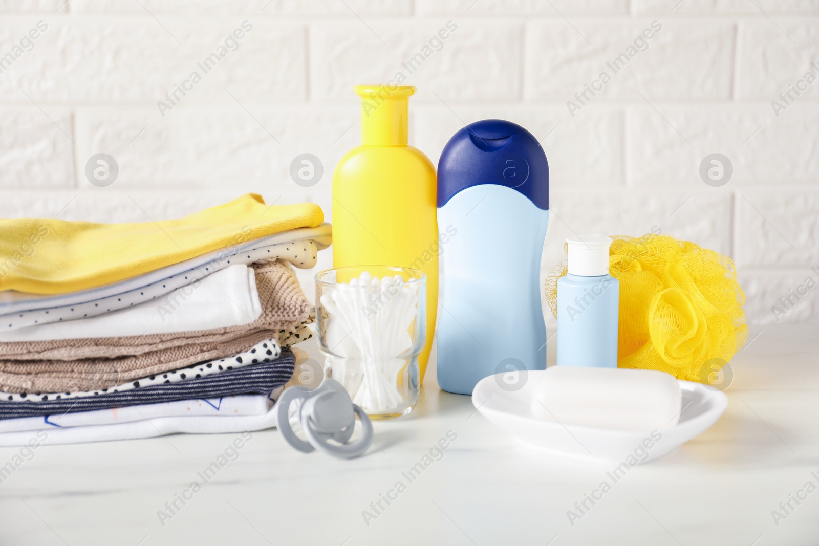 Photo of Different baby clothes and accessories on table near brick wall