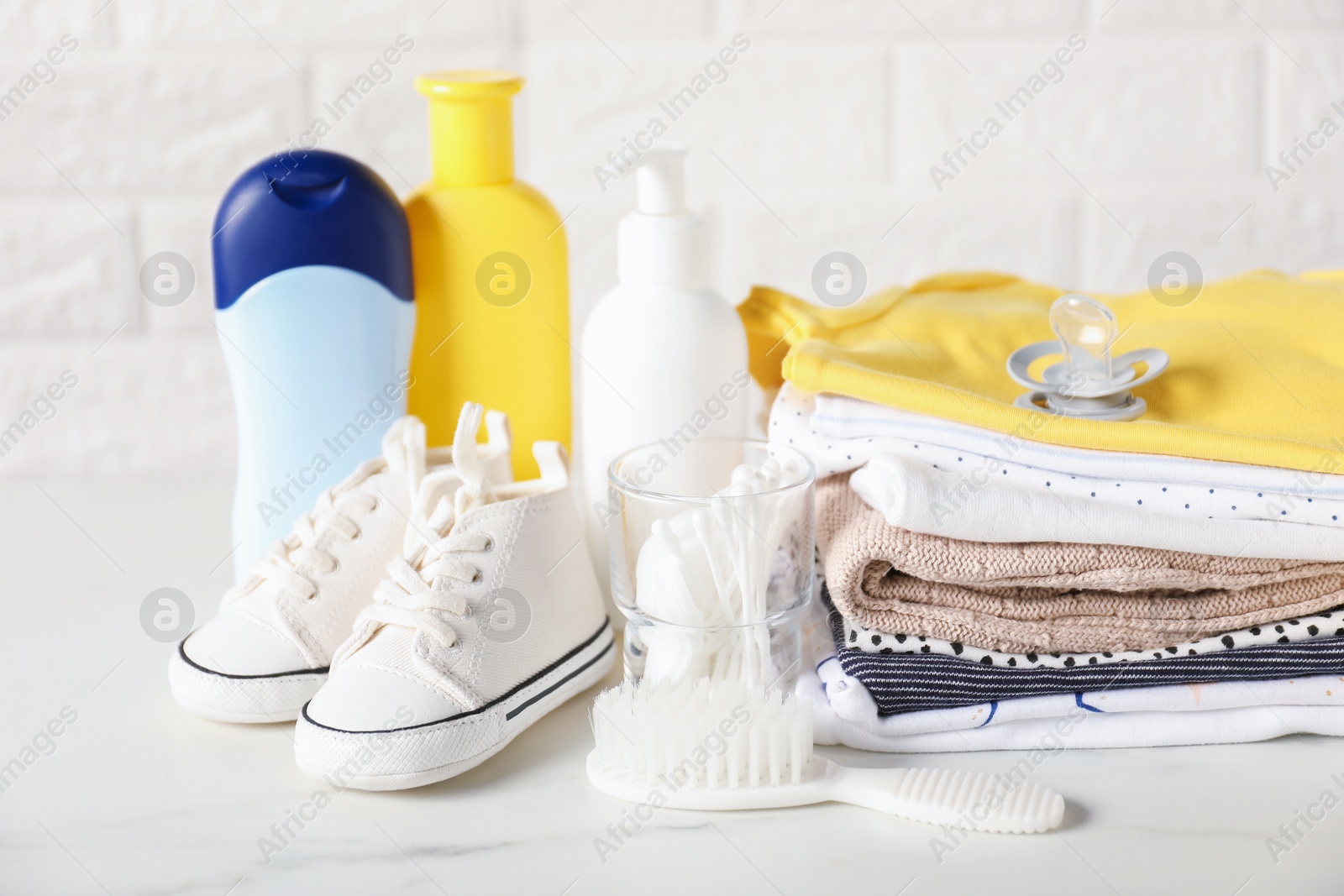 Photo of Different baby clothes and accessories on table near brick wall