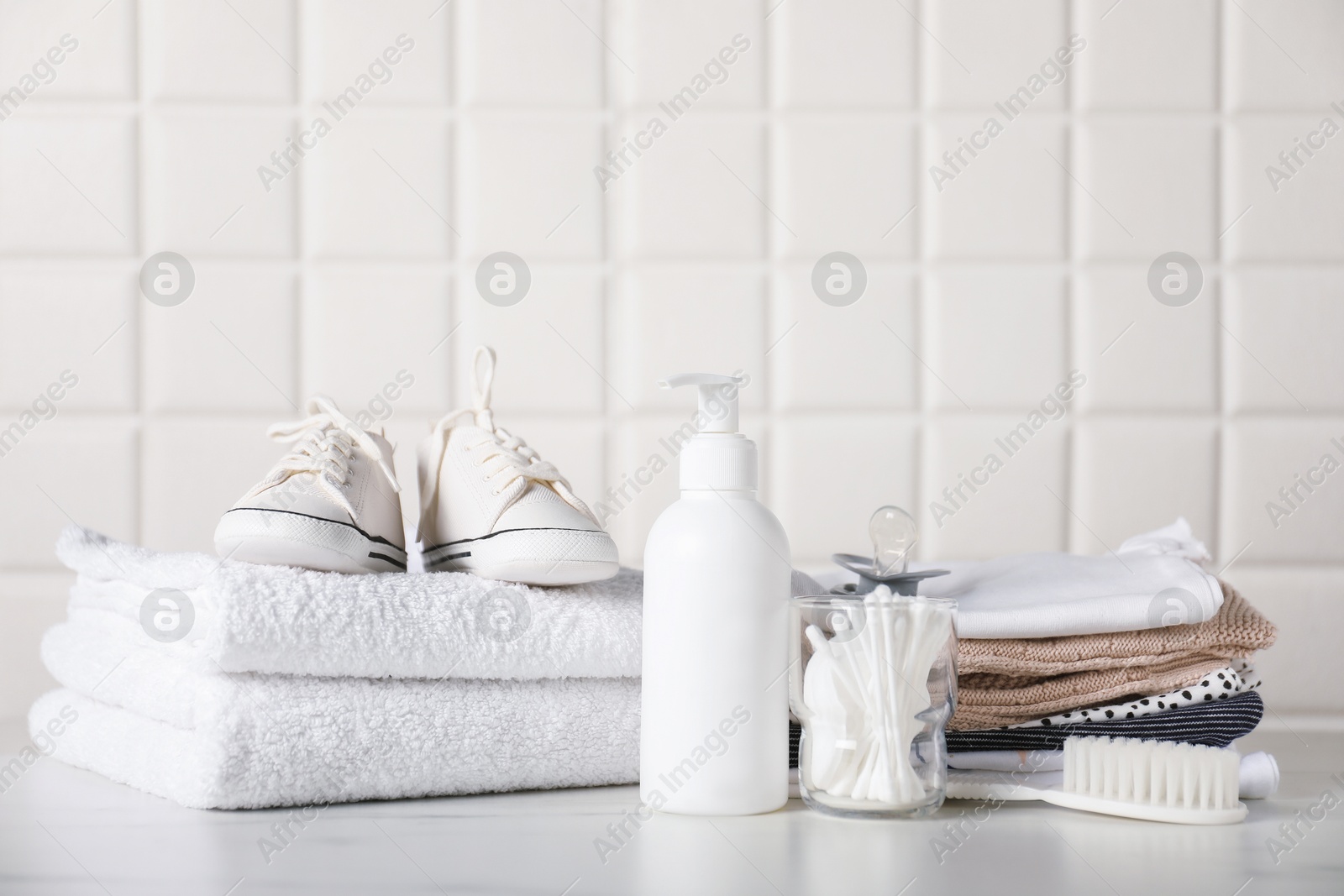 Different baby clothes and accessories on table near tiled wall Photo of Different baby clothes and accessories on table near tiled wall