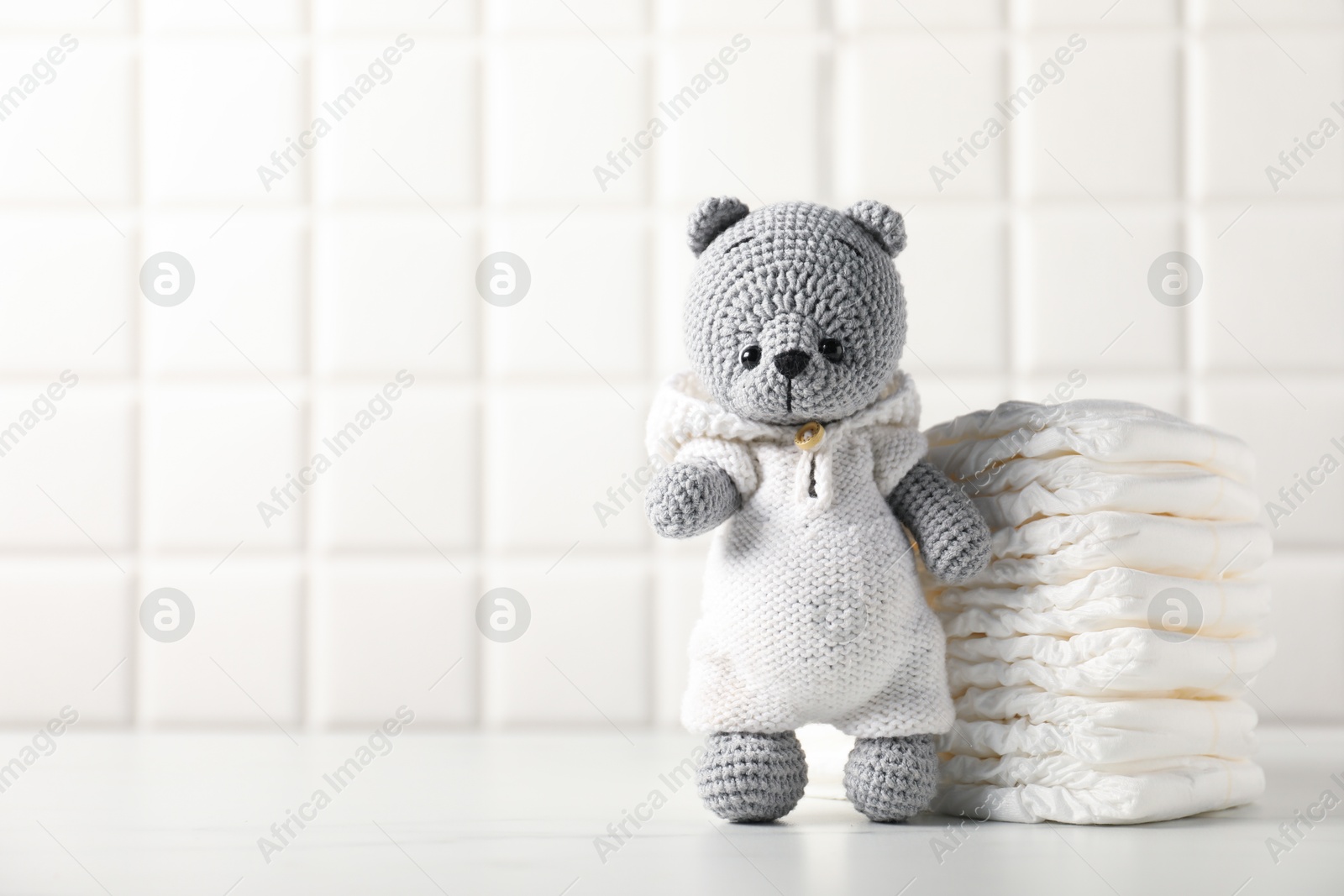 Baby diapers and toy bear on white table near tiled wall. Space for text Photo of Baby diapers and toy bear on white table near tiled wall. Space for text