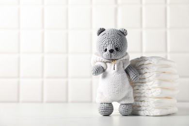 Photo of Baby diapers and toy bear on white table near tiled wall. Space for text