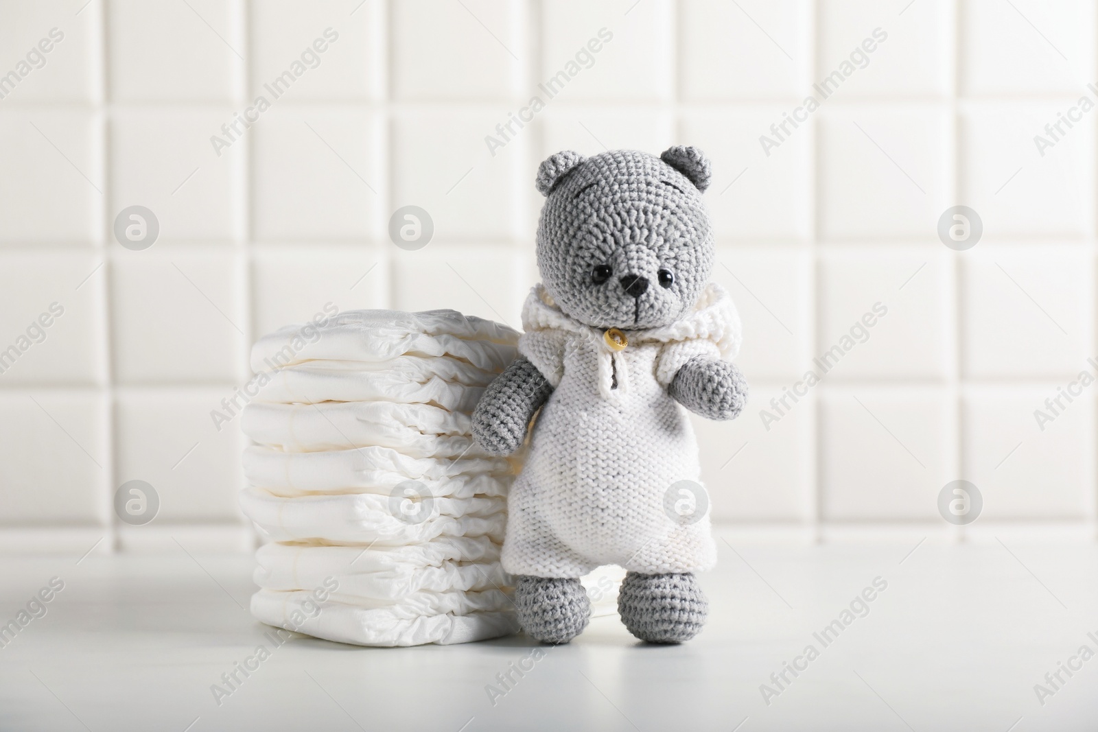 Baby diapers and toy bear on white table near tiled wall Photo of Baby diapers and toy bear on white table near tiled wall