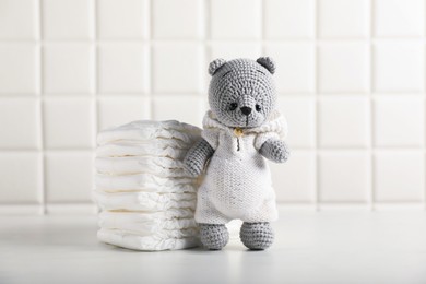 Photo of Baby diapers and toy bear on white table near tiled wall