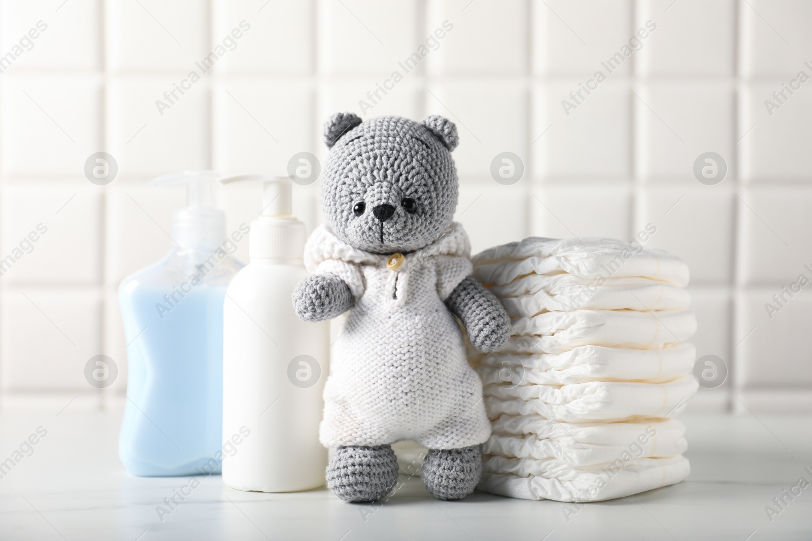 Photo of Many different baby accessories and toy bear on table near tiled wall