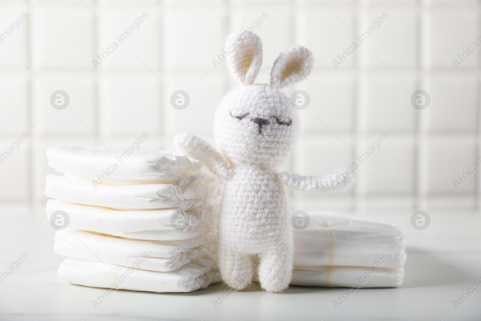 Photo of Baby diapers and toy bunny on white table near tiled wall