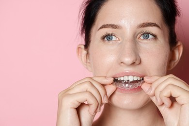 Photo of Woman wearing dental aligner on pink background, closeup. Space for text