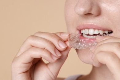 Photo of Woman wearing dental aligner on beige background, closeup