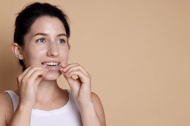 Photo of Woman wearing dental aligner on beige background. Space for text