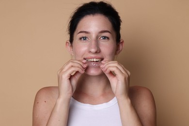 Photo of Young woman wearing dental aligner on beige background