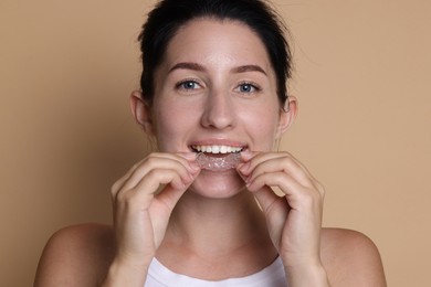Photo of Young woman wearing dental aligner on beige background